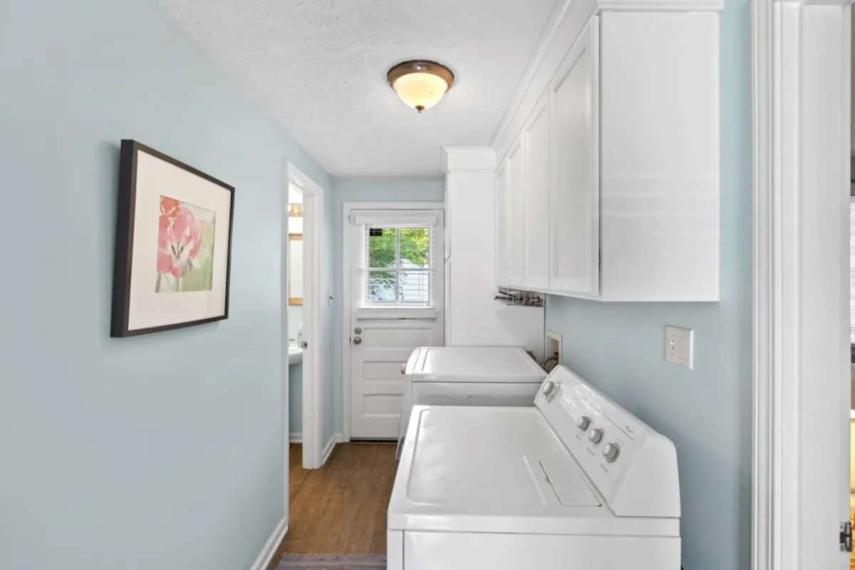 An inviting and practical laundry area featuring a washing machine, dryer, flower artwork, and a doorway letting in natural light. The space is tidy and efficient, offering a glimpse of how household tasks can be managed with ease during a stay.
