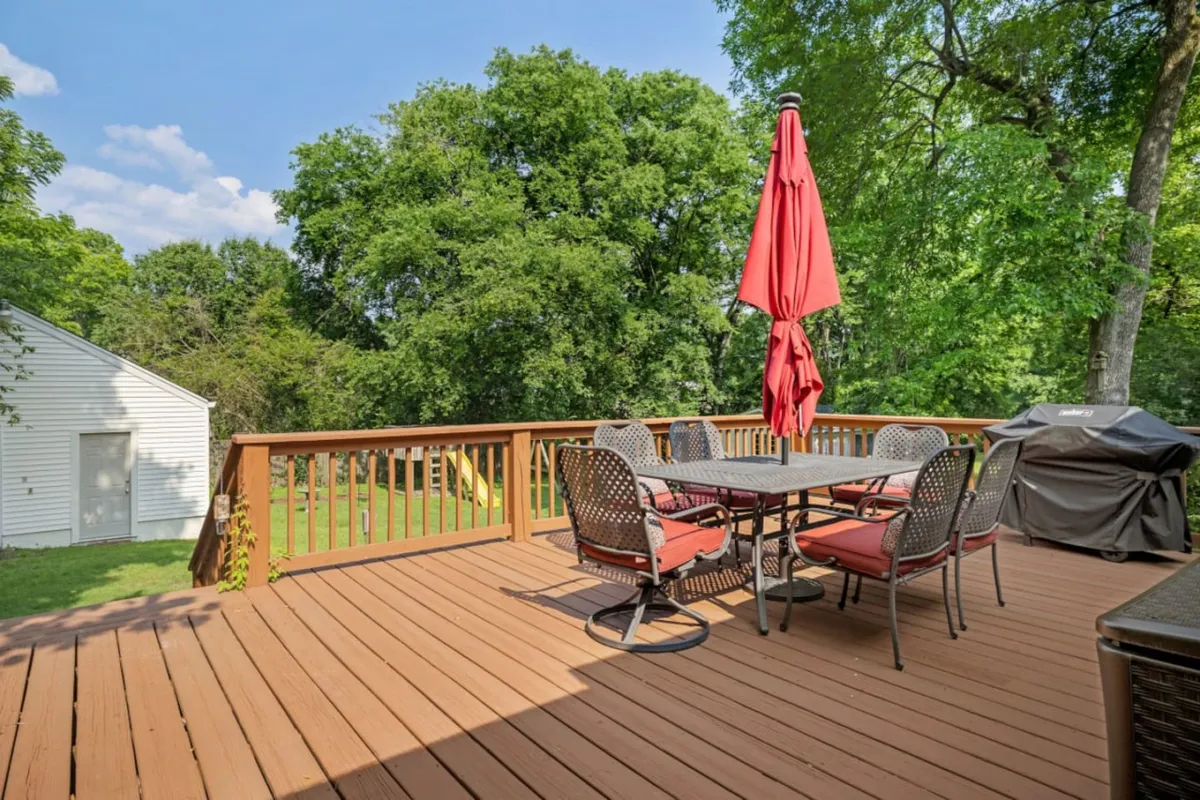 This image features a spacious wooden deck set amidst lush greenery, with a dining table shaded by an umbrella. The deck is ideal for outdoor gatherings, barbecues, and relaxing with friends or family. The natural surroundings and inviting setup evoke a sense of comfort and enjoyment.