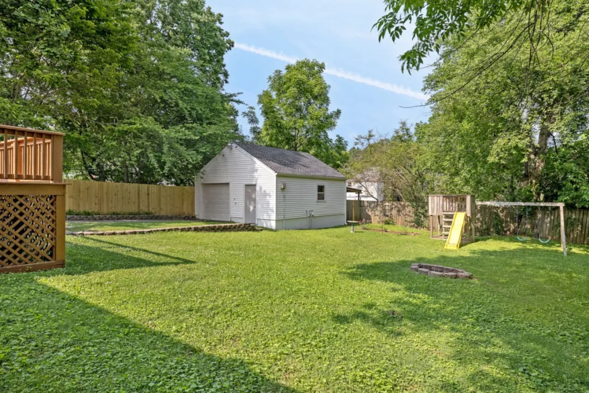 A wide shot of a green, fenced yard with a swingset, storage shed, and visible deck area. Children can be seen playing, and the space is clearly set up for both family fun and outdoor relaxation. The image captures the fire pit area and highlights possible activities like storytelling and barbecues.